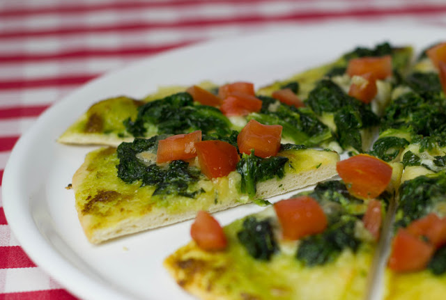 freshly sliced ​​pizza with pesto, spinach, garlic oil and diced tomatoes